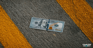 A hundred-dollar bill lying on an asphalt road between two yellow warning lines, symbolizing the financial penalties and regulatory action taken against ReadyBet for breaching Australia's BetStop self-exclusion rules.