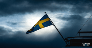 The Swedish flag waves against a cloudy, stormy sky, symbolizing the regulatory uncertainty facing the Swedish online gambling market.