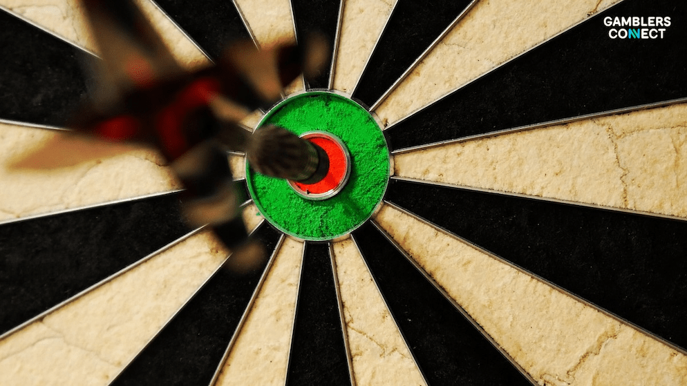 Darts world champion Luke Littler focused at the oche, preparing to throw a dart during a professional match, with event branding visible.