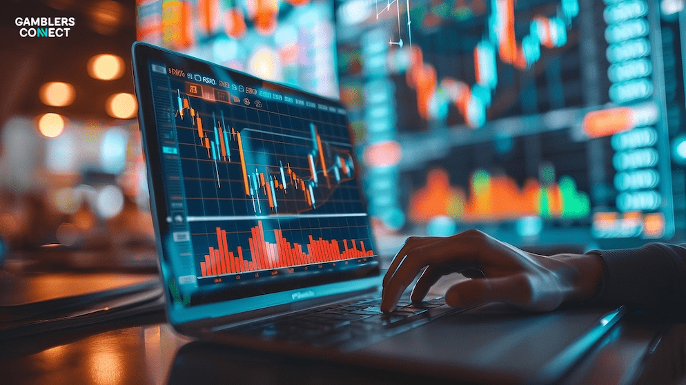 A close-up view of a person's hand typing on a laptop keyboard, with the screen displaying detailed financial candlestick charts and graphs, indicating market analysis and performance. In the blurred background, larger financial data displays are visible, suggesting a dynamic trading or analytical environment. The "Gamblers Connect" logo is visible in the top left corner.