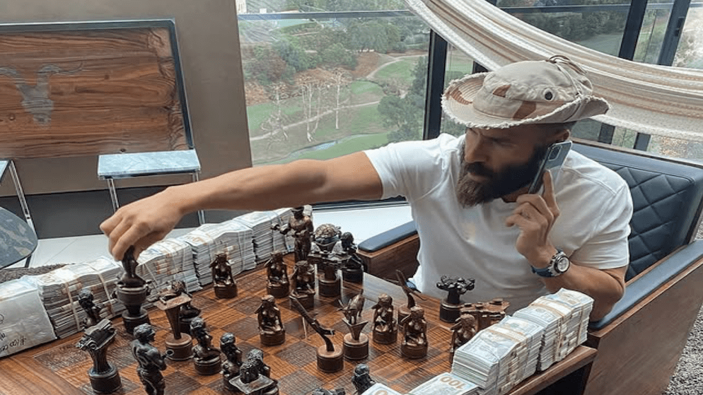 Dan Bilzerian playing chess with money around him depicting his net worth