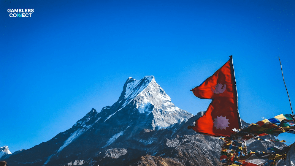 The flag of Nepal and traditional prayer flags with a Himalayan mountain in the background, representing the nation at the center of a crisis in its iGaming market.
