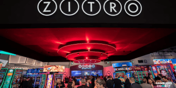 The Zitro brand name displayed prominently above a vibrant and crowded casino exhibition booth, featuring numerous slot machines and attendees under bright red circular lights, symbolizing Zitro's industry presence and commitment.