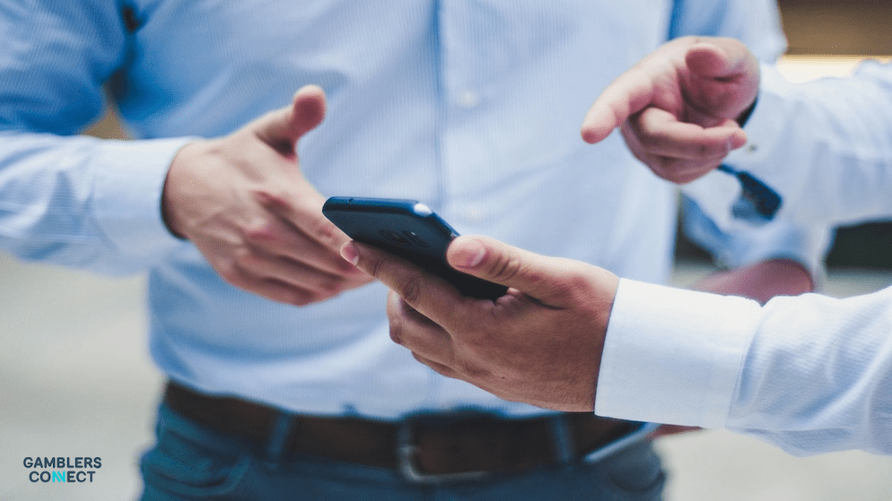 Two businessmen discussing a financial offer or takeover bid, with one pointing at a smartphone held by the other, symbolizing corporate negotiations or a takeover proposal such as the one by Kjerulf Ainsworth.