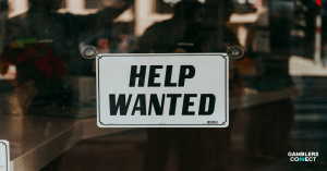 A "HELP WANTED" sign displayed prominently on a glass door, symbolizing BetBlocker's urgent request for assistance in identifying international responsible gambling resources.