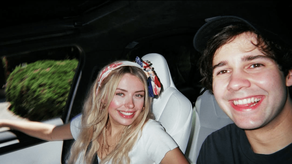 Corinna Kopf smiling next to David Dobrik in a car, reflecting their early association with the Vlog Squad that helped launch her career. This image is relevant to understanding the foundation of Corinna Kopf's net worth.