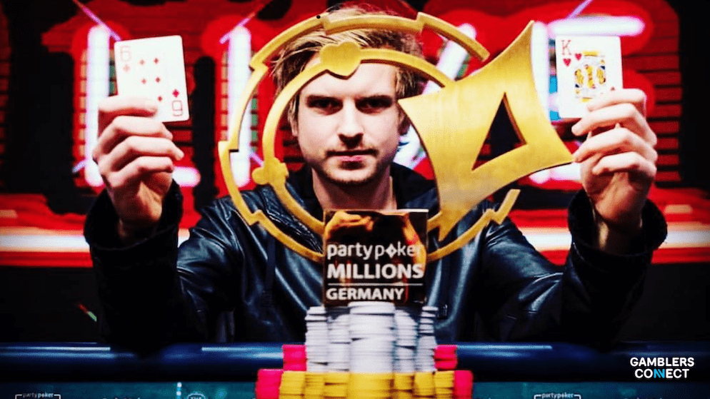 Isildur1 proudly holding up his winning poker cards and the partypoker Millions Germany Main Event trophy, with stacks of chips.