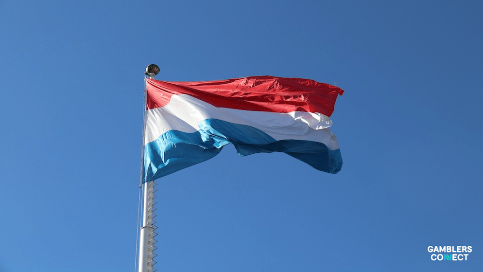 The red, white, and light blue flag of Luxembourg fluttering, symbolizing the ongoing internal discussions about a state-run online gambling model.