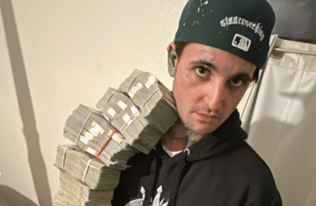 Professional gambler Mikki Mase holding numerous large stacks of cash on his shoulder, a visual representation of the massive gambling winnings he claims are the source of the mikki mase net worth.