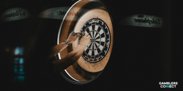 Close-up of a player's hands pulling three darts from a bullseye on a dartboard, symbolizing the precision and rising popularity of darts betting reported by Entain.