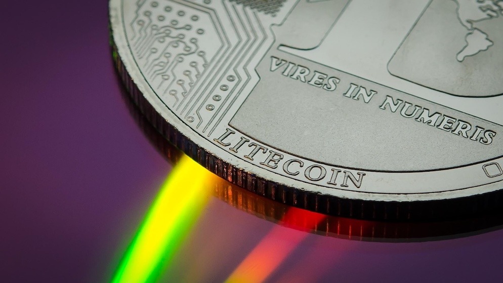 A close-up of a silver Litecoin coin with microchip circuitry details reflecting multicolored light, symbolizing decentralized technology and altcoin market activity.