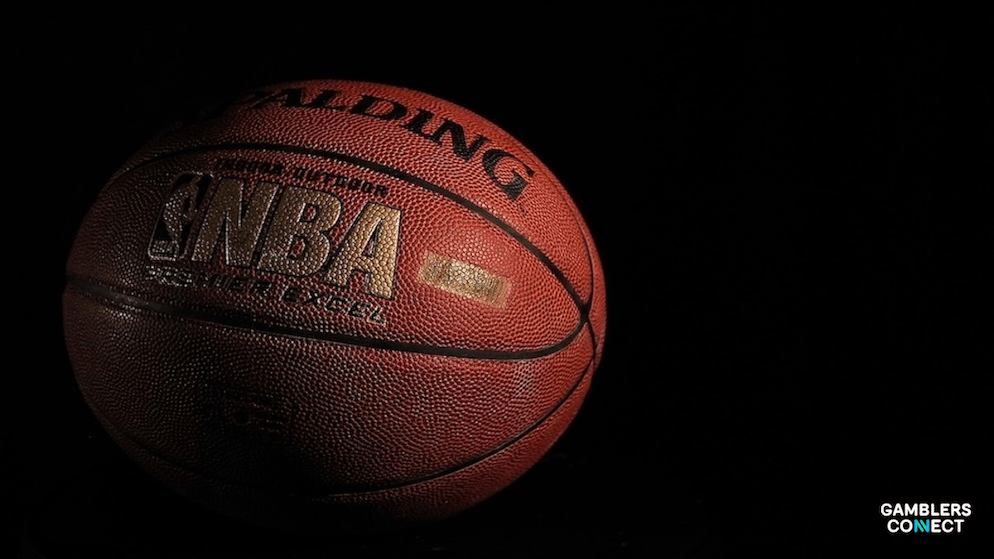 A close-up shot of an NBA basketball, partially in shadow, illustrating the serious nature of the ongoing gambling investigation impacting the league.