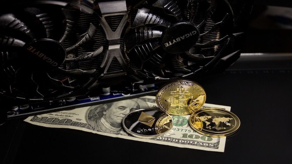 A mining GPU background with physical Bitcoin, Ethereum, and Ripple coins on a dollar bill, illustrating the diversified portfolios of dogecoin xrp btc holders.