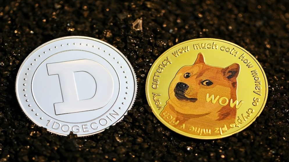 A close-up shot of a gold Dogecoin and a silver crypto coin placed on dark black gravel, symbolizing the connection between Scrypt-based coins.