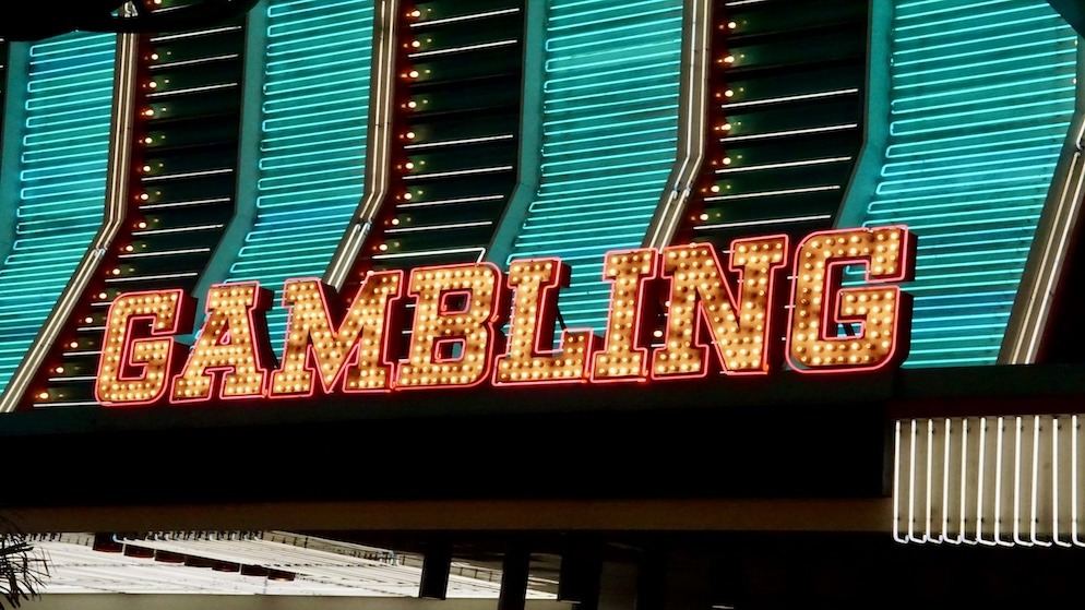 A vibrant neon sign brightly lighting up the word "GAMBLING" in marquee-style lettering, representing the booming market and its powerful advertising presence.