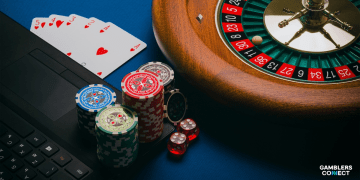 Close-up of a roulette wheel, casino chips, and playing cards resting on a laptop keyboard, symbolizing online gambling variety.