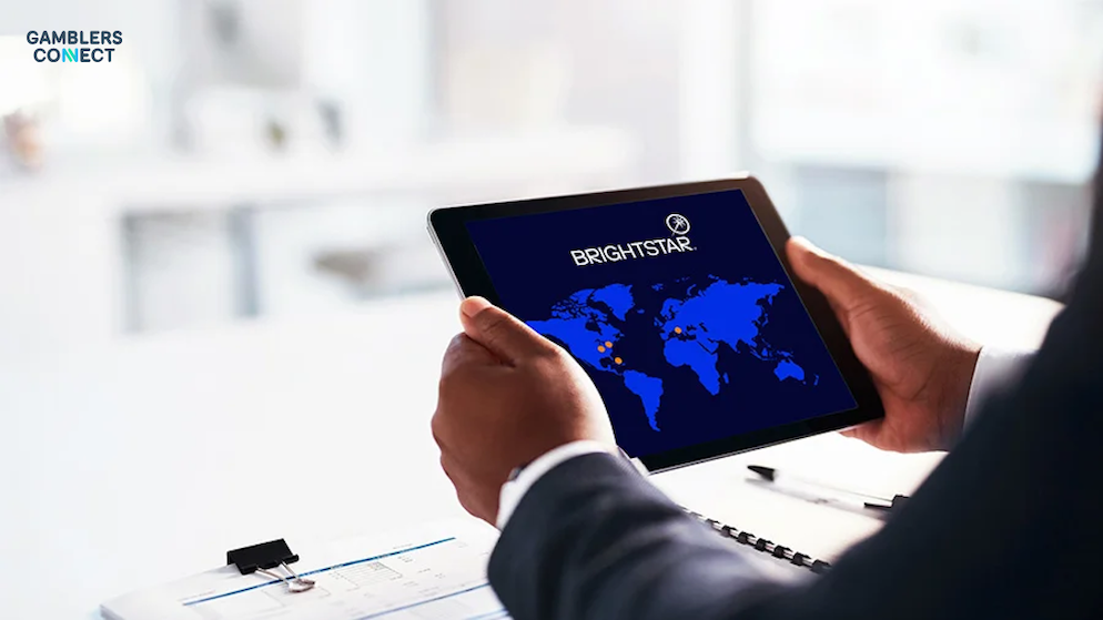 A detailed product shot of the Brightstar Retailer Pro S2 lottery terminal sitting on a retail counter, displaying a Lotterywest instant ticket menu on the screen.