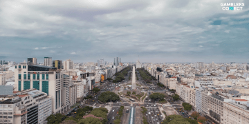 An aerial drone shot of the Obelisk and 9 de Julio Avenue in Buenos Aires, Argentina, representing the jurisdiction where the Provincial Institute of Lottery and Casinos (IPLyC) is cracking down on 300 unregulated betting sites.