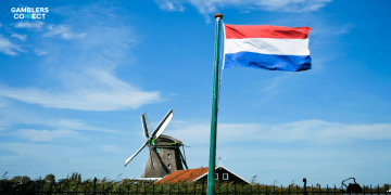 A photograph of the Dutch flag and a traditional windmill under a blue sky, symbolizing the Netherlands where the Dutch Gambling Authority (KSA) recently held a roundtable with online operators to discuss player protection and duty of care obligations.