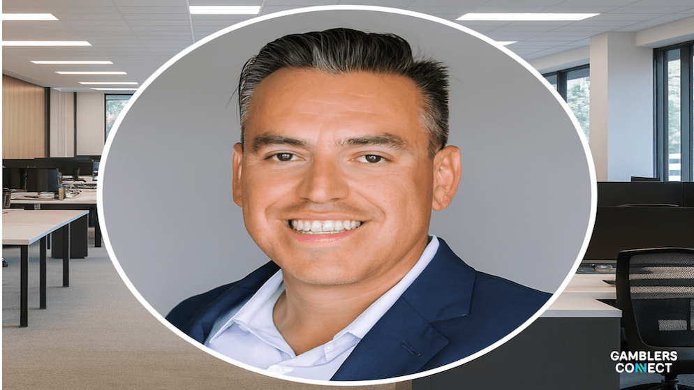 Hector Fernandez, former CEO of Aristocrat Gaming, smiling in a navy blue suit against a grey background.