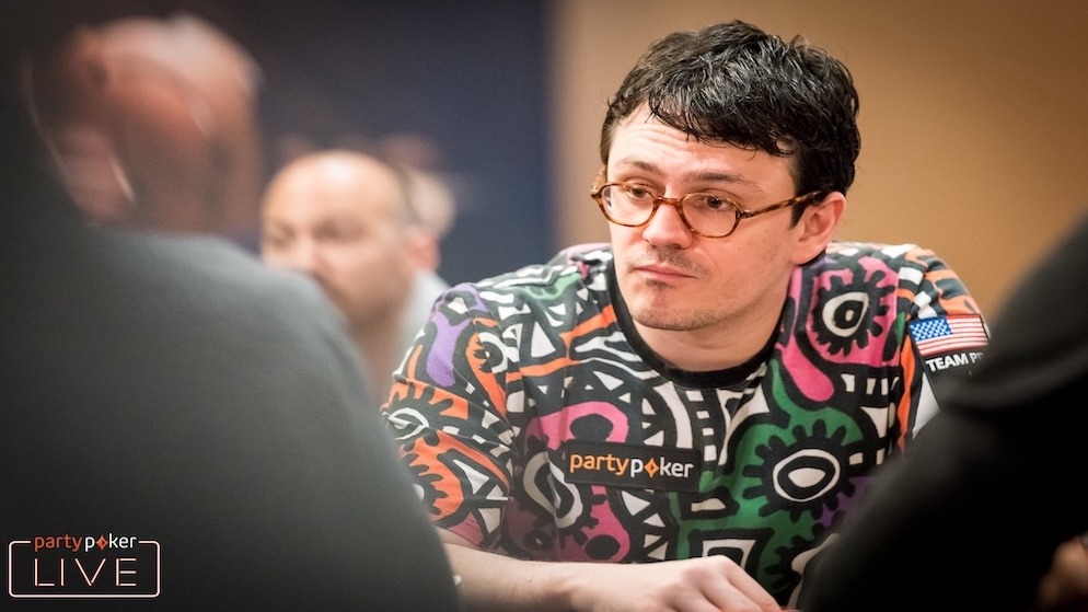 Isaac Haxton wearing glasses and a colorful t-shirt with a PartyPoker logo, looking intently to the side while seated at a poker table during a live event.