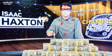 Isaac Haxton wearing a face mask and a Super High Roller Bowl ring, standing behind a large pyramid of cash and his winning hand of 7-8 clubs. A sign behind him reads "ISAAC HAXTON CHAMPION $2,760,000".