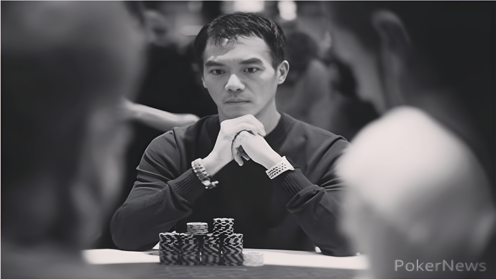 A black and white close-up shot of John Juanda with his hands clasped and a serious expression, staring down an opponent across a stack of chips.