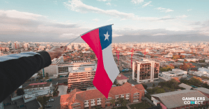 A hand holding the Chilean flag overlooking a city skyline at sunset, symbolizing the new regulatory cooperation agreement between Chile's aPAL and the UK's BGC.