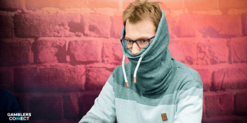 Christoph Vogelsang wearing his iconic outfit with a pulled-up hoodie and a scarf covering his mouth and neck to hide physical tells during a high-pressure hand.