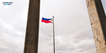 The national flag of the Philippines flying against a cloudy sky between two concrete pillars, representing the regulatory changes announced by PAGCOR for the country's gaming industry.