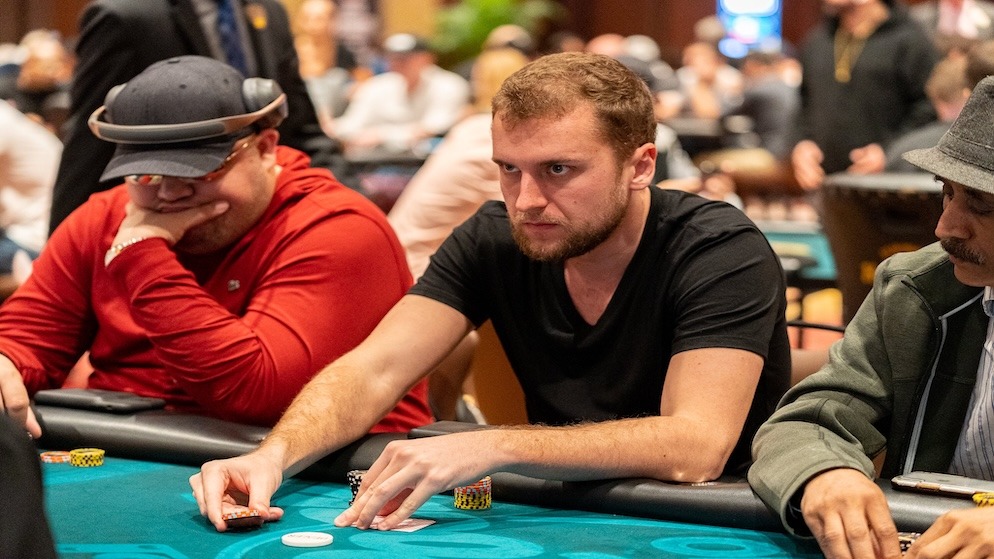 A focused Ryan Riess stacking chips at a poker table during a high-stakes tournament, wearing a black t-shirt and looking intensely at the action.