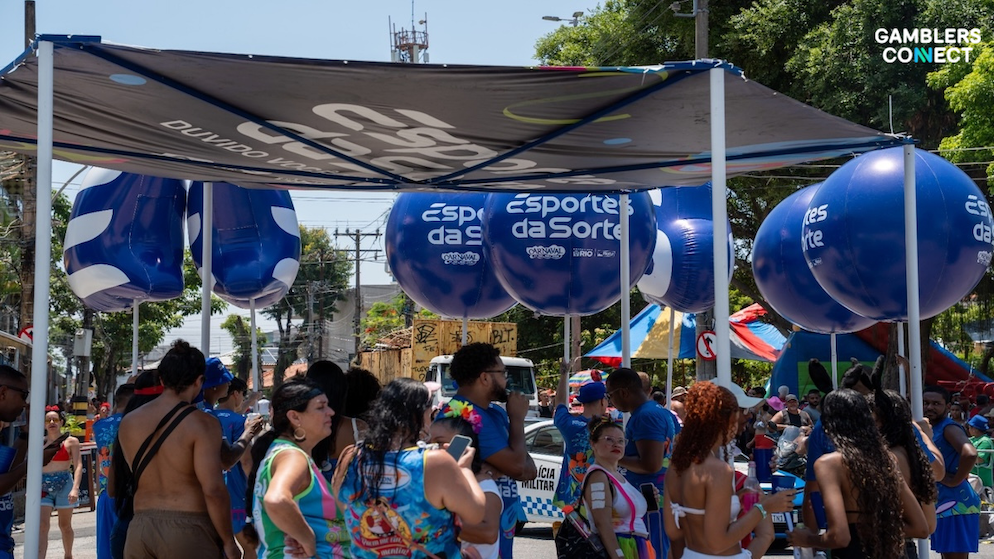 Pedestrians walking through a blue Esportes da Sorte branded cooling station during the heat of Brazil's street carnival.