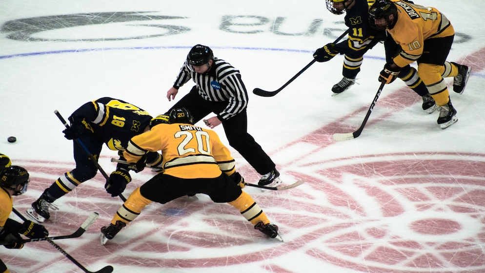 A high-angle shot of a hockey face-off at center ice, illustrating the start of one of the three 20-minute periods in a professional North American game.