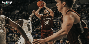 A college basketball player in a red jersey taking a jump shot during a high-stakes game.