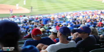 A person monitoring sports betting data and financial charts on multiple screens while using a smartphone calculator.