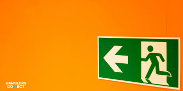 Mike Raffensperger in a navy suit leaning on a broadcast desk with a discovery+ microphone in an empty stadium.