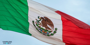 The national flag of Mexico waving vibrantly against a clear, pale blue sky.