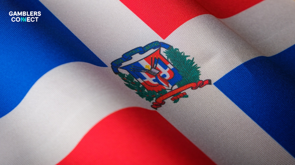 The national flag of the Dominican Republic (white cross with red and blue quadrants and the national coat of arms) waving in the wind.