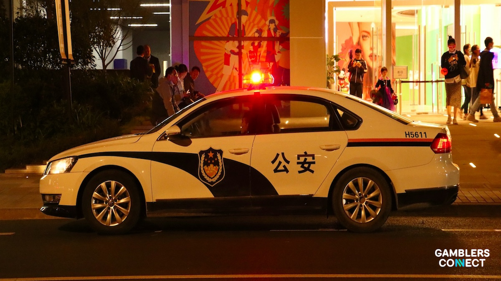 A white Hong Kong police car with "公安" (Public Security) written on the side and red flashing lights, parked at night in a city area.