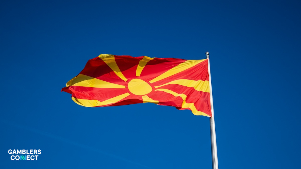 The national flag of North Macedonia (red with a yellow sun) waving from a pole against a clear, deep blue sky.