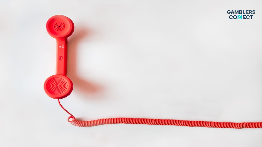 An overhead minimalist shot of an isolated classic red telephone receiver attached to a coiled plastic wire over a clean white table.