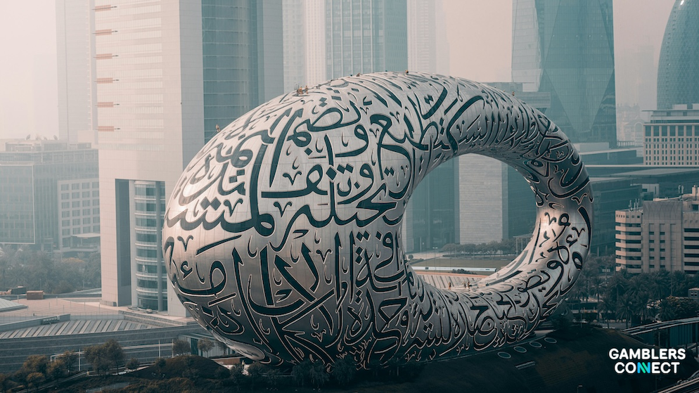 The iconic curved silver structure of the Museum of the Future positioned in front of high-rise commercial office towers in Dubai.