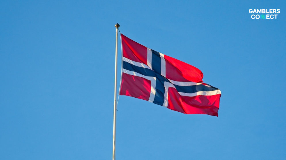 The red, white, and blue Norwegian national flag billowing dynamically on an outdoor flagpole under clear afternoon sunlight.