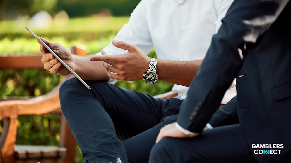 A close-up side view of two business professionals sitting outdoors in a park, with one individual pointing down at the screen of a slim silver digital tablet.