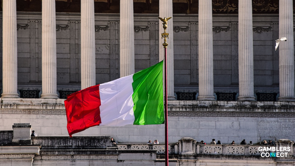The national tricolor flag of Italy rippling smoothly under bright sunlight against a classical Roman building architecture.