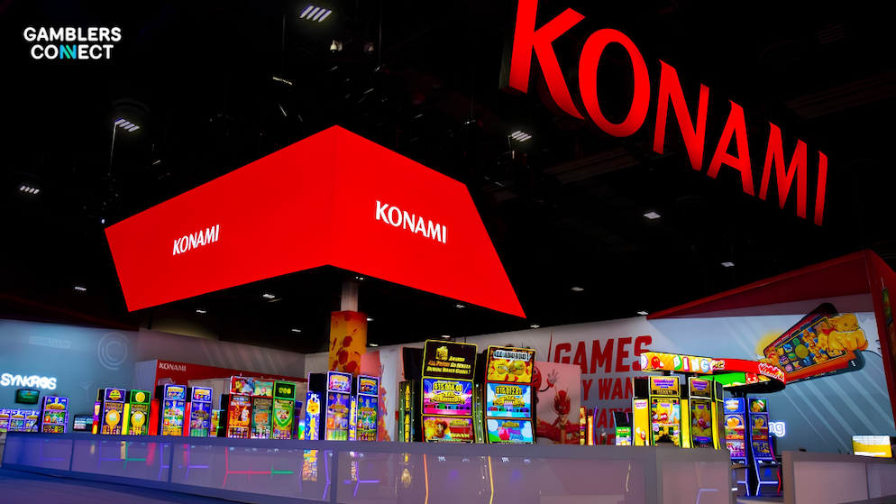 A premium red neon Konami corporate logo display hanging from the ceiling structure of an international land-based gaming exposition pavilion.