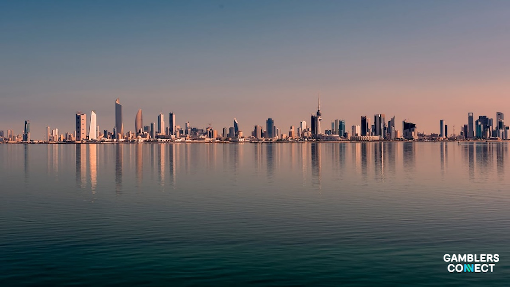 A wide panoramic landscape shot of the coastal skyline of Kuwait City, showing multiple modern skyscrapers and high-rise commercial office towers reflecting perfectly onto calm sea waters.