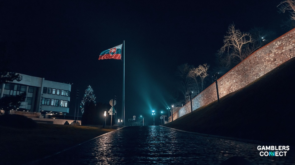 The red, white, and blue national flag of Slovakia flying under directional spotlights against historic building architecture in Bratislava.