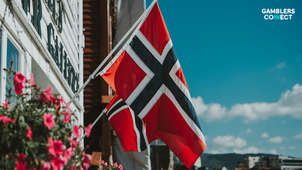 Progress Party Keynote Outlines Blueprint to Dismantle Norway's Gambling Monopoly 1 The red, white, and blue Scandinavian flag of Norway blowing smoothly on a pole against a crisp blue sky and soft cloud backdrop layer.