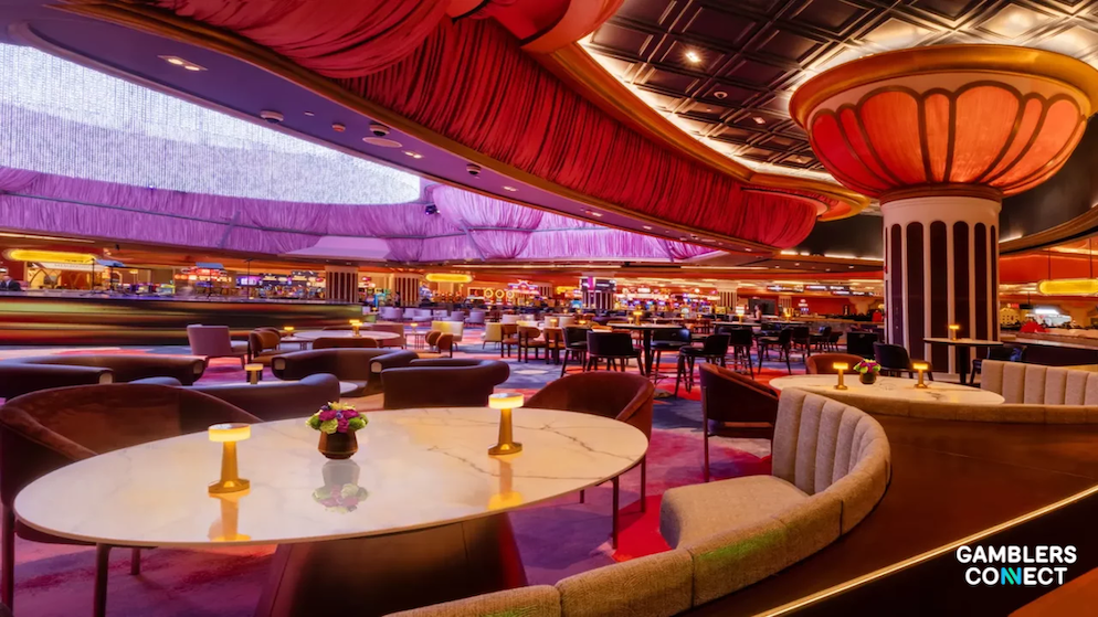 An upscale resort lounge area with elegant curved booths, warm ambient table lighting, and a view of a spacious casino floor layout under custom light fixtures.